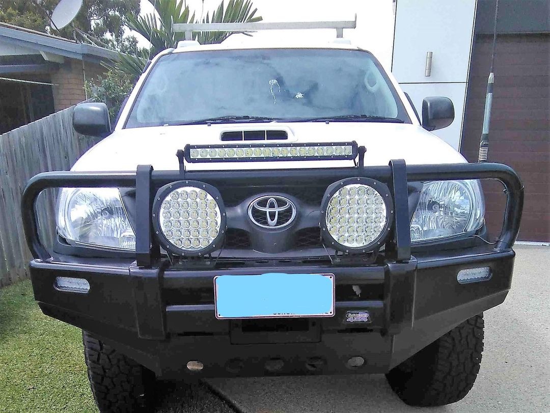 A white Toyota Hilux fitted with a steel bull bar, driving lights and an LED light bar